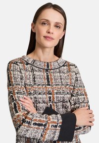 Sweater with a textured, patterned design featuring black, gray, brown, and orange colors. Rounded neckline and long sleeves with black cuffs.