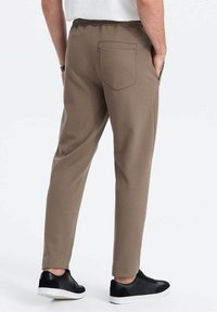 Bruine, gestructureerde, slim-fit broek met een elastische tailleband en een achterzak, gecombineerd met zwarte sneakers. Casual ontwerp geschikt voor dagelijks gebruik.