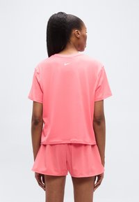 Σετ αθλητικό με κοντά μανίκια και σορτς σε έντονο ροζ χρώμα. Το ύφασμα είναι λείο· το τοπ διαθέτει διακριτικό λογότυπο της Nike στην πίσω πλευρά στο λαιμό.