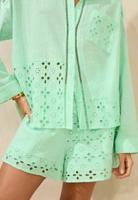Mintgroene twee-delige set met een knoopshirt met een geborduurd patroon en bijpassende shorts met een laser-cut ontwerp.