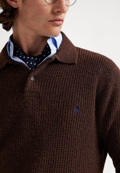 Brun strikket polosweater med teksturert mønster, med en blå brodert logo på brystet og klassisk krage.
