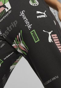 Svart tyg med olika Puma-logotyper, text inklusive "Sportstyle," "Puma Sportstyle," och abstrakta gröna och rosa former.