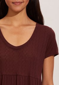 T-shirt bordeaux avec un col en V, des manches courtes et un tissu texturé avec un motif subtil. Matière douce et légère avec une coupe décontractée.