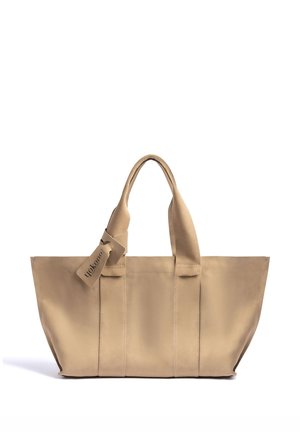 Bolsa de tela beige con asas dobles y una pequeña etiqueta de tela unida a una de las asas, sobre un fondo blanco liso.