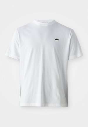 Witte T-shirt met korte mouwen en ronde hals, met een groen krokodillenlogo op de linkerborst, afgebeeld tegen een effen witte achtergrond.