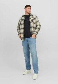 Geruite flanellen shirt in beige en marineblauw, zwart T-shirt, lichtblauwe jeans en witte sneakers. Heeft twee borstzakken en een losse pasvorm.