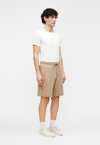 Smėlio spalvos šortai su vertikaliu tekstūriniu raštu, tampri liemuo ir raišteliai. Dėvimi su balta marškinėlių ir šviesiais sportbačiais.