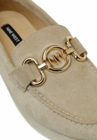 Mocasines de ante beige con herrajes circulares en tono dorado y detalles de acento. Punta redondeada y borde cosido, con una textura sutilmente brillante.
