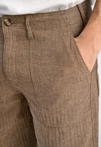 Bruna herringbone-tygbyxor med en nätt passform, med sidofickor och knappstängning, som uppvisar en subtil texturerad design.