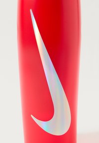 Röd sportvattenflaska med matt yta och en stor iriserande Nike swoosh-logotyp. Slät textur och avsmalnande form.