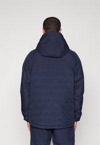 Marinblå huva jacka med quiltad textur, framzip och elastiska mudd, designad för värme och skydd mot väder och vind.