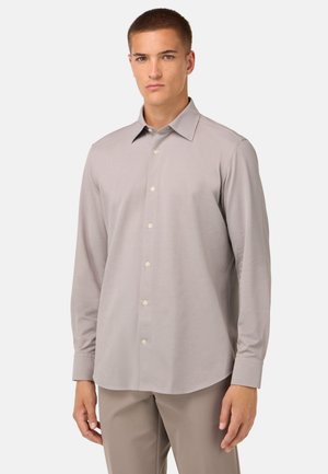 Chemise à manches longues gris clair avec un col pointu, une fermeture à boutons et une texture de tissu lisse. Présente un ourlet incurvé et des poignets standards.
