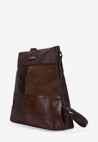 Mochila de cuero marrón con texturas mixtas, que presenta paneles lisos, de ante y grabados. Diseño delgado y rectangular con correa ajustable.
