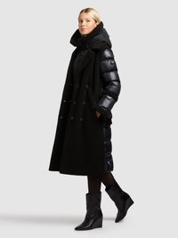Fekete, dupla soros kabát bolyhos textúrával, fényes bélelt belső réteggel párosítva. A megjelenést fekete, ék talpú csizmák egészítik ki.