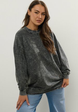 Overmaatse grijze sweatshirt met een stone-wash textuur, geribbelde ronde hals en lange mouwen. Gepaarde met lichtblauwe denim jeans.