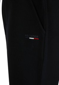 Zwarte sweatshirt met een klein "HECHTER" logo geborduurd in grijs, met rode, witte en blauwe strepen. Zacht materiaal met een gestructureerd oppervlak.