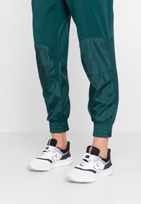 Turkusowe spodnie dresowe z elastycznymi mankietami w połączeniu z czarno-białymi trampkami. Trampki mają logo „N” oraz teksturowane siateczkowe akcenty.