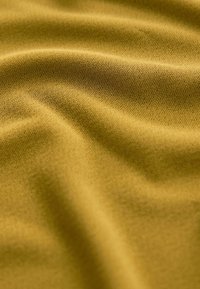 Tissu doux jaune moutarde avec une texture fine en maille, présentant des plis et des ombres délicates.