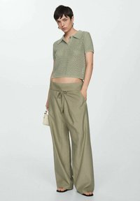 Top verde chiaro, a maniche corte, in maglia leggera con colletto abbinato a pantaloni olive verdi, a vita alta e a gamba larga. Include una borsa piccola.