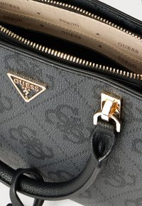 Sac à main synthétique noir avec motif texturé, garniture dorée, fermeture éclair et emblème de marque. L'intérieur est doublé beige avec des logos.