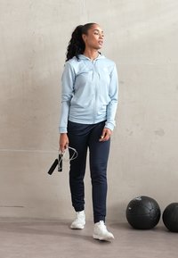 Svetlo modrá mikina na zips s klokaním vreckom, námornícke športové nohavice a biele tenisky. Hladká tkanina, priliehavý dizajn, súčasťou sú aj švihadlo.