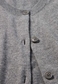 Grauer Cardigan aus weichem Strickmaterial mit rundem Ausschnitt, drei grauen Knöpfen und einem kleinen Knopfloch-Detail.