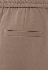 Rjavo blago z gladko teksturo, z elastiko v pasu in enim vodoravnim zadnjim žepom. Preprost in minimalističen dizajn.