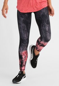 Legginsy w czarno-różowy wzór z teksturowanym gradientem, dopasowany krój, połączone z czarnymi butami sportowymi.