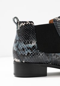 Botín de tobillo de piel de serpiente negro y azul con paneles laterales elásticos y un tacón bajo negro. Con lengüeta trasera para facilitar su uso. Superficie suave y texturizada.