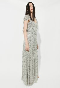 Silberne mit Pailletten verzierte Abendkleid mit fließender Silhouette, kurzen Rüschensäumen und tiefem V-Ausschnitt. Lang und bodenlang mit strukturierter Stoff.
