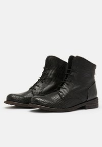Botines negros perforados con punta redonda, cordones en la parte delantera y una superficie texturizada. Suela de madera marrón en contraste y un detalle de marca sutil.