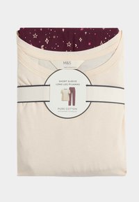 Pijamas de algodón en color crema y burdeos de manga corta y pierna larga, con un estampado estrellado en los pantalones, empaquetados con una etiqueta.