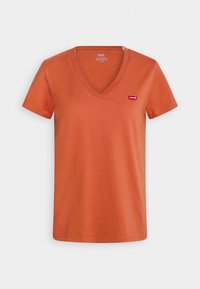 T-shirt a maniche corte con scollo a V color arancione ruggine, con una piccola etichetta rossa del logo Levi's sul petto in alto a sinistra, mostrata su uno sfondo semplice.