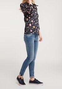 Blusa floral azul marino con mangas largas, con botones en la parte delantera, combinada con unos jeans pitillo de color azul claro y zapatillas azul marino con suelas blancas.