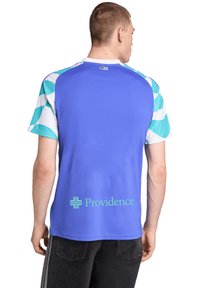 Mand iført en blå sportsjersey med teal- og hvidmønstrede ærmer og "Providence" logo på den nederste del af ryggen, vender væk fra kameraet.