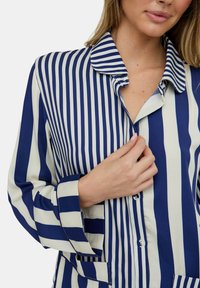 Blau-weiß gestreifte Bluse mit Kragen, langen Ärmeln und Knopfleiste. Der Stoff hat eine glatte Textur.