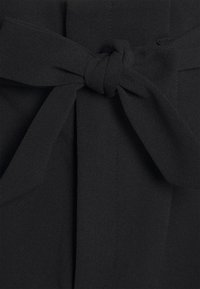 Tissu noir à texture lisse, présentant un détail de nœud noué à la taille. Le matériau a un drapé doux et un léger éclat.