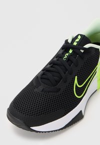 Black athletic shoe with neon green Nike swoosh, black laces, breathable mesh upper, and white sole with neon green heel accents.