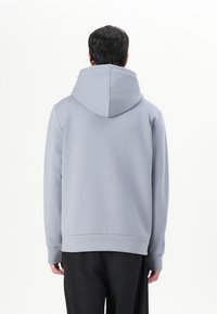 Sudadera gris con una gran capucha redondeada, mangas largas y puños acanalados. Confeccionada en un material suave y ligero. La cinturilla termina a la altura de la cadera.