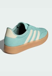 Light blue suede sneaker with three white stripes, beige heel cap, and tan rubber sole; features round toe and lace-up design.