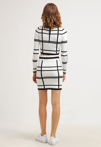 Ensemble composé d'un crop top blanc et d'une jupe avec des lignes noires en grille, au design ajusté, à manches longues et avec un détail de nœud dans le dos. Associé à des baskets blanches.