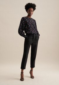 Blusa nera a maniche lunghe con stampa floreale colorata, abbinata a pantaloni neri su misura e sandali neri con tacco a stiletto.