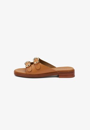 Tankleurige lederen slipper met twee gouden gespbanden en lage houten hak, zijaanzicht op witte achtergrond.