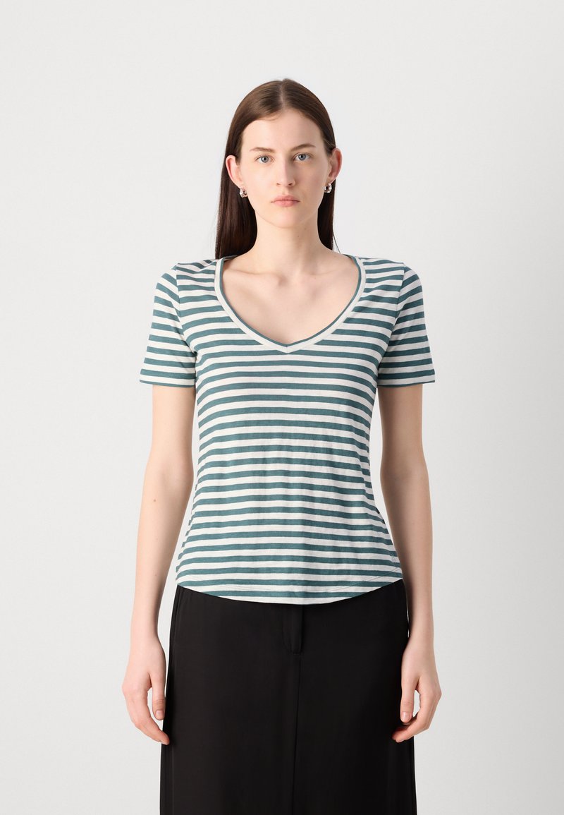 Zielono-biała, w paski koszulka z krótkim rękawem i dekoltem w serek, wykonana z miękkiej bawełny, o dopasowanym kroju, w zestawieniu z czarnymi spodniami o szerokich nogawkach.