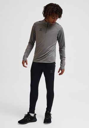 Maglia sportiva grigia a maniche lunghe con collo a zip a un quarto, abbinata a leggings neri aderenti. Presenta il logo del marchio su entrambi i capi.