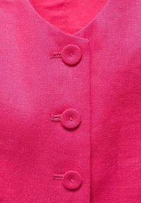 Gros plan d’un vêtement en tissu rose avec trois boutons recouverts du même tissu, alignés verticalement près de la couture centrale.