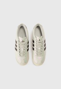 Ténis desportivos verde-claro com riscas pretas, couro texturizado e gola almofadada. Apresentam fecho de atacadores e logótipo na lingueta.