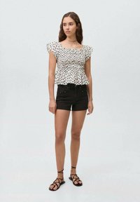 Top bianco senza spalle con pois neri, maniche corte e orlo peplum abbinato a pantaloni corti in denim neri e sandali con strappi.