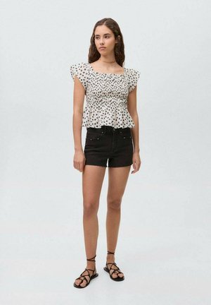 Haut blanc à épaules dénudées avec des pois noirs, manches courtes, et ourlet peplum associé à un short en denim noir et des sandales à lanières.
