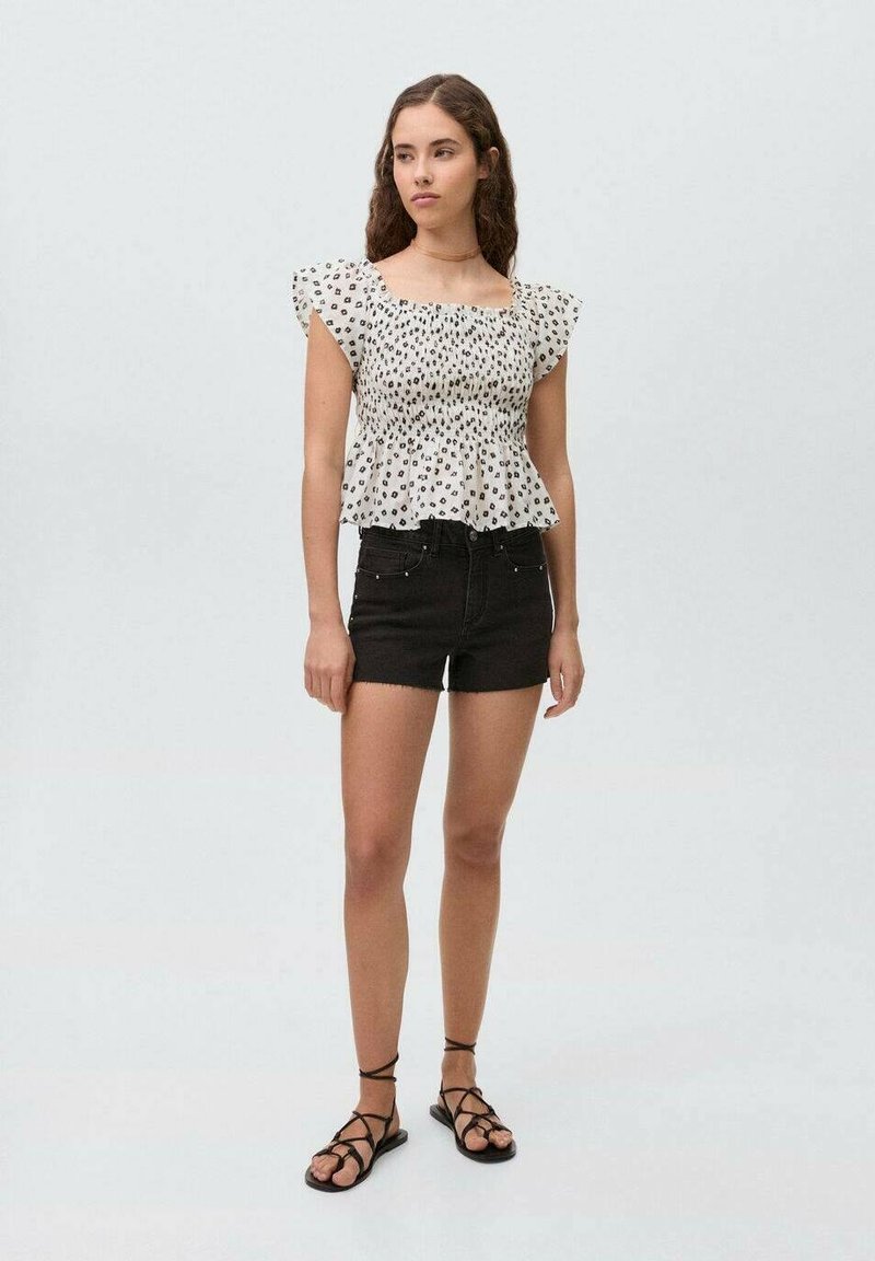 Top bianco senza spalle con pois neri, maniche corte e orlo peplum abbinato a pantaloni corti in denim neri e sandali con strappi.
